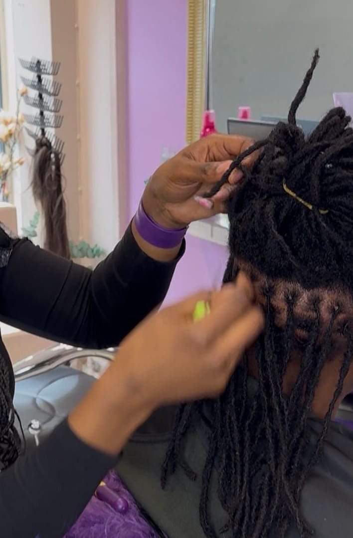 Närbild på händer som gör retwist på locs i salongen